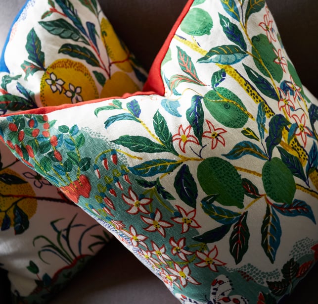 Two throw pillows with bright, colorful designs with fruit, leaves, and flowers used by Jasmin Reese in a living room design. 