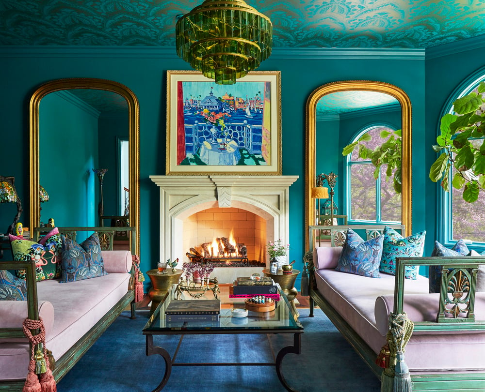 A large Moroccan-style living room in pink, blue, and turquoise with a white marble fireplace with large gold-framed mirrors on either side - living room design by Jasmin Reese Interiors, Chicago, USA.