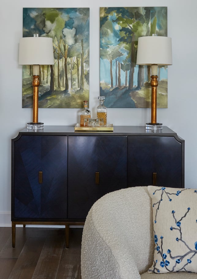 A blue and black, art deco bar with two copper candlestick lamps with cream lampshades in front of panel artwork of a stand of trees - living room design by Jasmin Reese Interiors, Chicago, USA. 