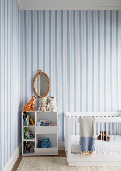 A baby's nursery with blue pinstriped wallpaper and white furniture designed by Jasmin Reese, Chicago. 