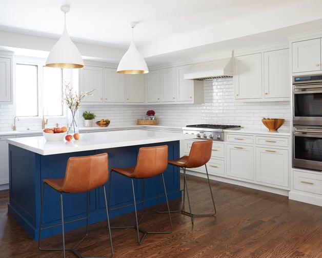 A large bright blue and white kitchen with orange barstools, interior design by Jasmin Reese, Chicago. 