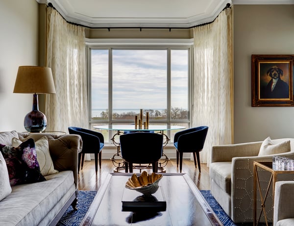 A view of a small dining area with blue circular chairs around a round glass and metal table with flowing lace floor-to-ceiling drapes - living room design by Jasmin Reese Interiors, Chicago, USA. 