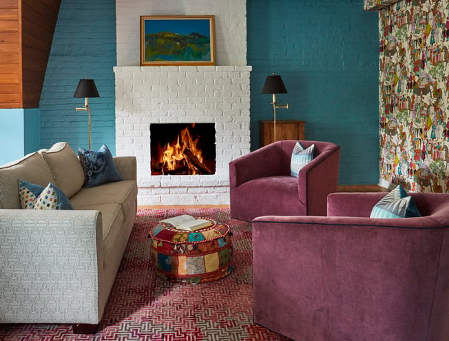 A seating area around a fireplace in a game room designed by Jasmin Reese, Chicago: turquoise brick, patchwork wallpaper and ottoman. 