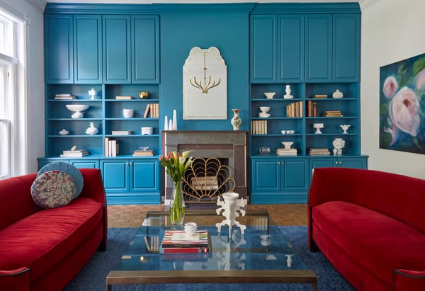 Two large bright red sofas and a turquoise built-in bookshelf with a glass coffee table and fireplace - living room design by Jasmin Reese Interiors, Chicago, USA. 