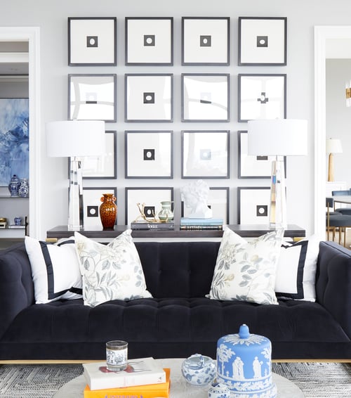 A closeup view of a long dark grey sofa with a long table with glass lamps in front of a collection of sixteen framed pictures of a black square with a white circle inside - living room design by Jasmin Reese Interiors, Chicago, USA.