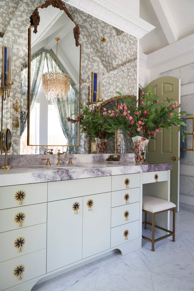 A close view of a marble top vanity with foil wallpaper and unique brass sunburst fixtures in a bathroom designed by Jasmin Reese, Chicago. 
