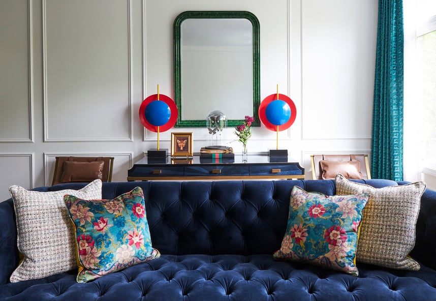 A bright blue velvet sofa with floral and tweed throw pillows with bright blue and red art on either side of a mirror in the background - living room design by Jasmin Reese Interiors, Chicago, USA. 