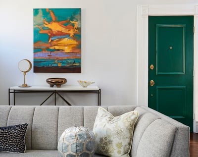 An abstract painting with bright orange and turquoise over a side table beside a tan sofa with interesting throw pillows - living room design by Jasmin Reese Interiors, Chicago, USA.