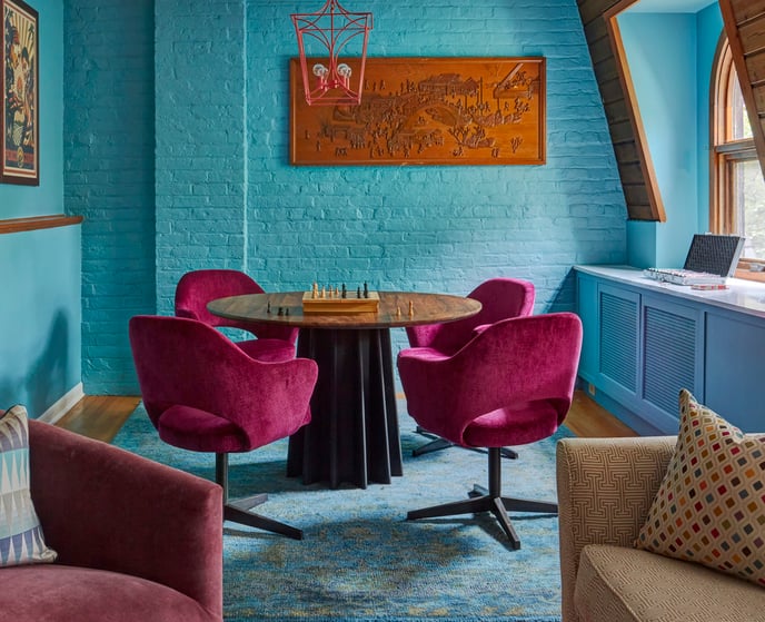 A game table with magenta velvet chairs against a turquoise brick wall in a game room designed by Jasmin Reese Interiors. 
