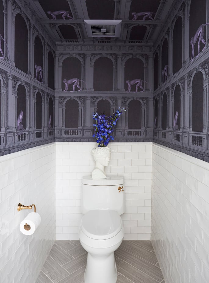 A white subway-tiled powder room with Roman archway monkey wallpaper designed by Jasmin Reese, Chicago. 