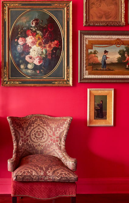 A small armchair in a dining room designed by Jasmin Reese with cherry red walls and Victorian paintings, Chicago. 
