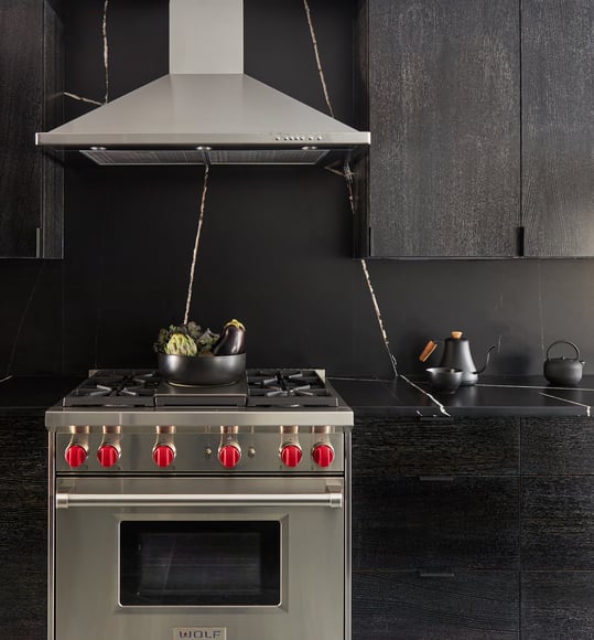 A black kitchen designed by Jasmin Reese with a stainless steel stove oven with red knobs, Chicago. 
