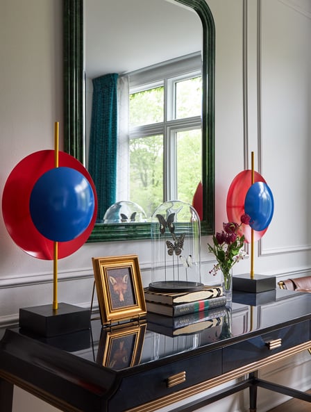 Unique bright red and blue circular art pieces on either side of a black enamel desk with butterflies under a glass dome and a small painting of a fox in a gold frame - living room design by Jasmin Reese Interiors, Chicago, USA. 