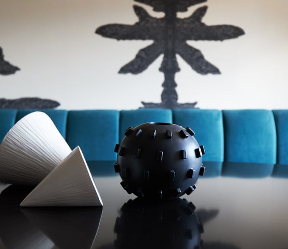 A dining room detail by Jasmin Reese: a black sphere with spikes and two textured white cones on a table, Chicago. 
