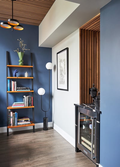 An built-in mini-fridge in a home office designed by Jasmin Reese: ladder shelf with books, unique corner sphere lamp. 