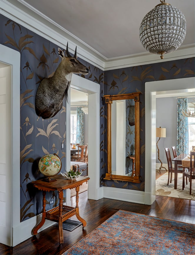 An entryway with taxidermy, an antique globe, an antique table, and a mirror with a grey and gold foil wallpaper - living room design by Jasmin Reese Interiors, Chicago, USA. 