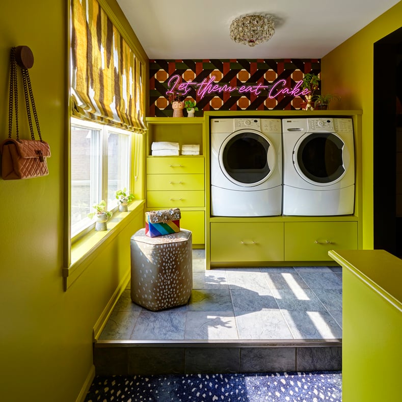 A frontal view of a laundry room with a side-by-side modern washer and dryer with chartreuse cabinetry and window treatment with 