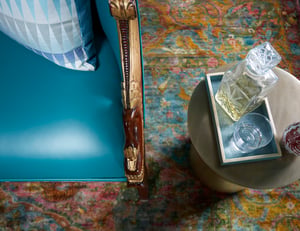 A detail of a carved wood design on a turquoise leather armchair next to a crystal decanter and glass on a brass table - living room design by Jasmin Reese Interiors, Chicago, USA. 