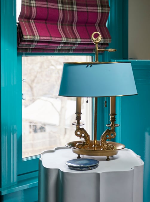 A detail of a turn-of-the-century brass lamp with a turquoise blue metal lampshade on a white enamel table - living room design by Jasmin Reese Interiors, Chicago, USA. 
