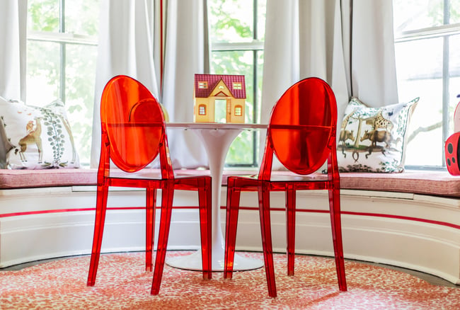 A retro white enamel table with a dollhouse and red acrylic chairs in a child's room designed by Jasmin Reese, Chicago. 