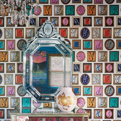 An ornate mirror with a mirrored frame on wallpaper with multiple paintings of rabbits on different colored backgrounds with gold frames - living room design by Jasmin Reese Interiors, Chicago, USA.