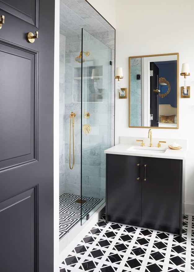 A small black and white tiled bathroom with a single sink and brass fixtures designed by Jasmin Reese, Chicago. 