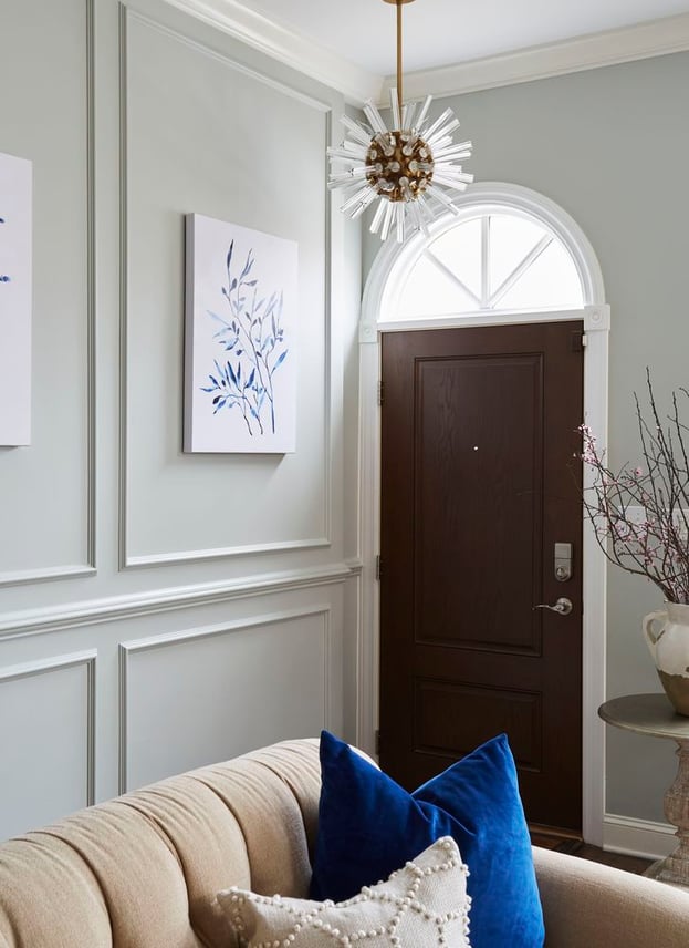A view of a dark wood front door from a tan sofa with blue and cream textured throw pillows - living room design by Jasmin Reese Interiors, Chicago, USA. 
