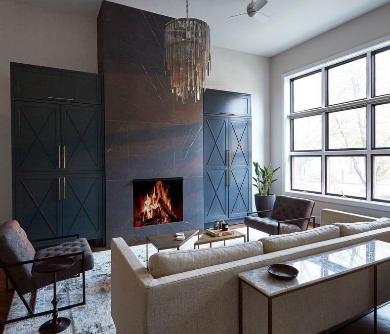 A large black marble floor-to-ceiling fireplace with built-in cabinets on either side inside a living room with a long tan sofa and grey modern armchairs - living room design by Jasmin Reese Interiors, Chicago, USA. 