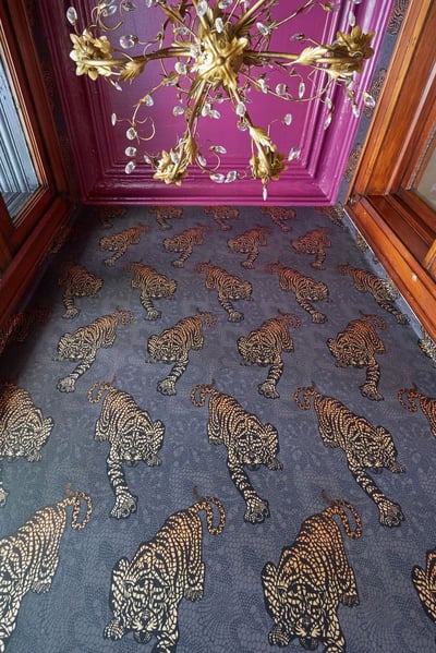 Looking up at a brass and crystal chandelier, a magenta ceiling, and black, grey, and gold foil wallpaper with tigers - living room design by Jasmin Reese Interiors, Chicago, USA. 