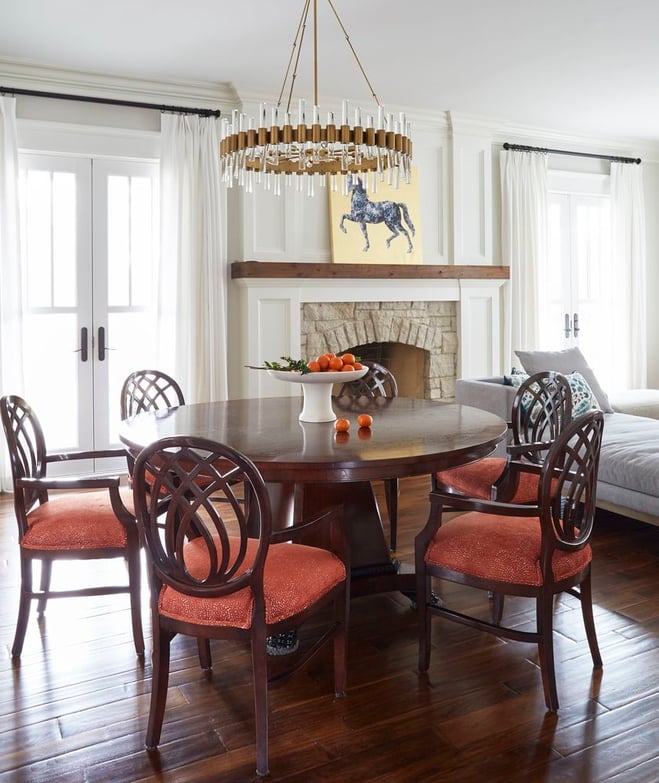 A dining room designed by Jasmin Reese with a round, traditional dining room table and red upholstered chairs. 