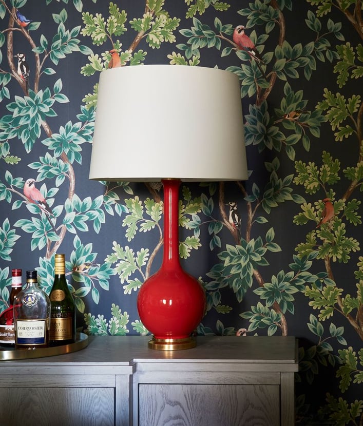 A vibrant red lamp in front of lively green leaves and black wallpaper by Jasmin Reese Interiors, Chicago, USA. 
