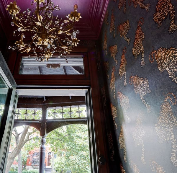 An entryway with a brass and crystal chandelier, a magenta ceiling, and black, grey, and gold foil wallpaper with tigers - living room design by Jasmin Reese Interiors, Chicago, USA. 