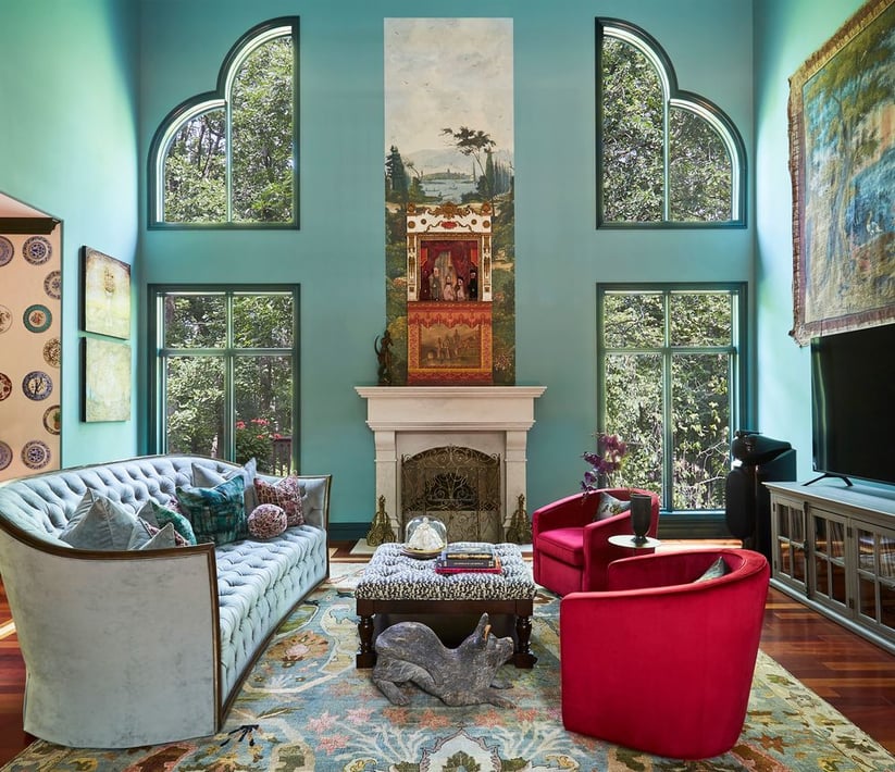 A level view of a large green living room with high ceilings with ornate windows that look out over trees outside - a Victorian sofa is upholstered in light blue to match the muted green tones - living room design by Jasmin Reese Interiors, Chicago, USA. 