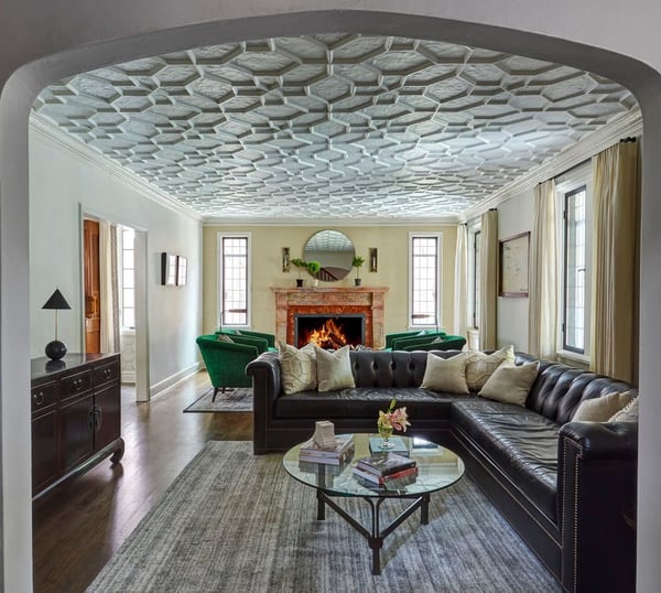 A traditional living room with a dark leather sectional sofa, and four green velvet circular armchairs in front of a large fireplace painted orange - living room design by Jasmin Reese Interiors, Chicago, USA. 