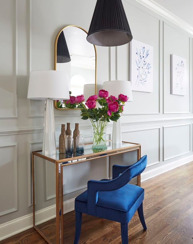 An open, bright entryway with a mirror and brass table with double glass lamps and a blue velvet armchair - living room design by Jasmin Reese Interiors, Chicago, USA. 