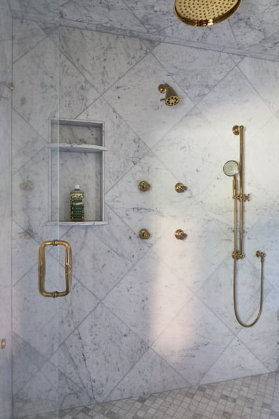 A view inside a large walk-in marble & brass shower in a bathroom designed by Jasmin Reese, Chicago. 