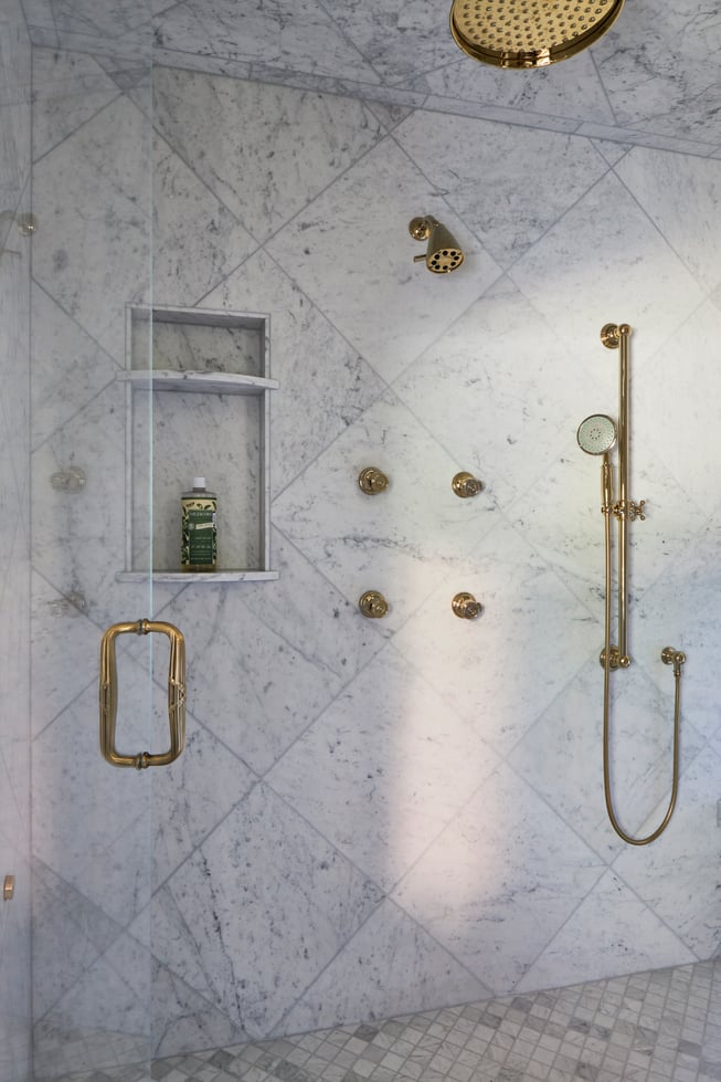 A view inside a large walk-in marble & brass shower in a bathroom designed by Jasmin Reese, Chicago. 